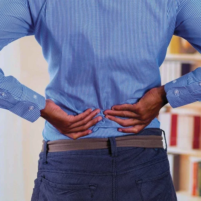 A person is shown from behind, holding their lower back, indicating possible discomfort or back pain.